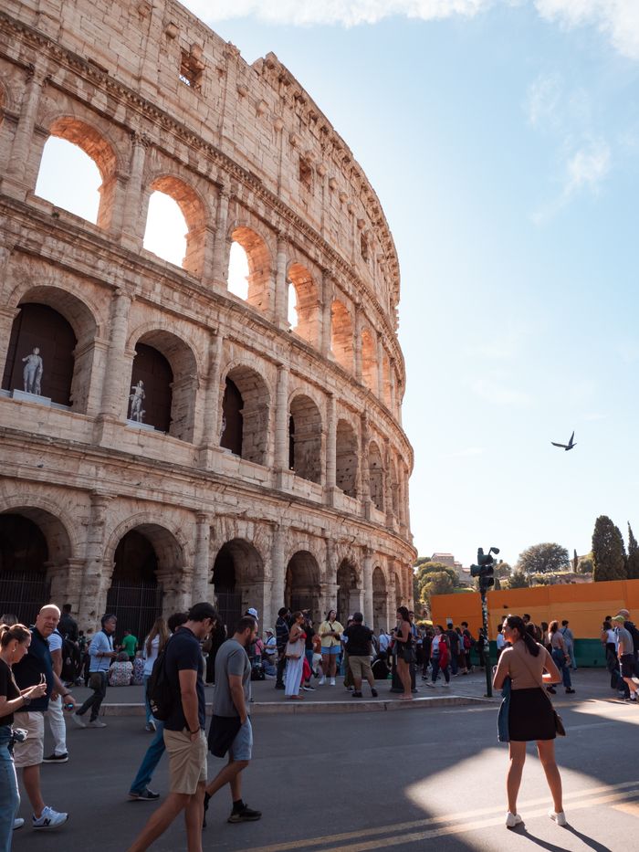 Crowd gathers around the Colosseum in Rome, capturing the ancient landmark under the sunny sky.