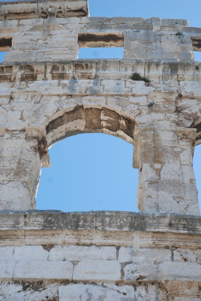 Close-up of the historic Pula Arena architecture under a clear blue sky.