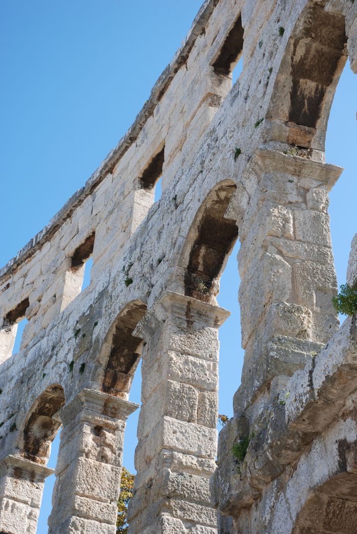 Close-up of the ancient Roman amphitheater arches in Pula, Croatia under a clear blue sky.